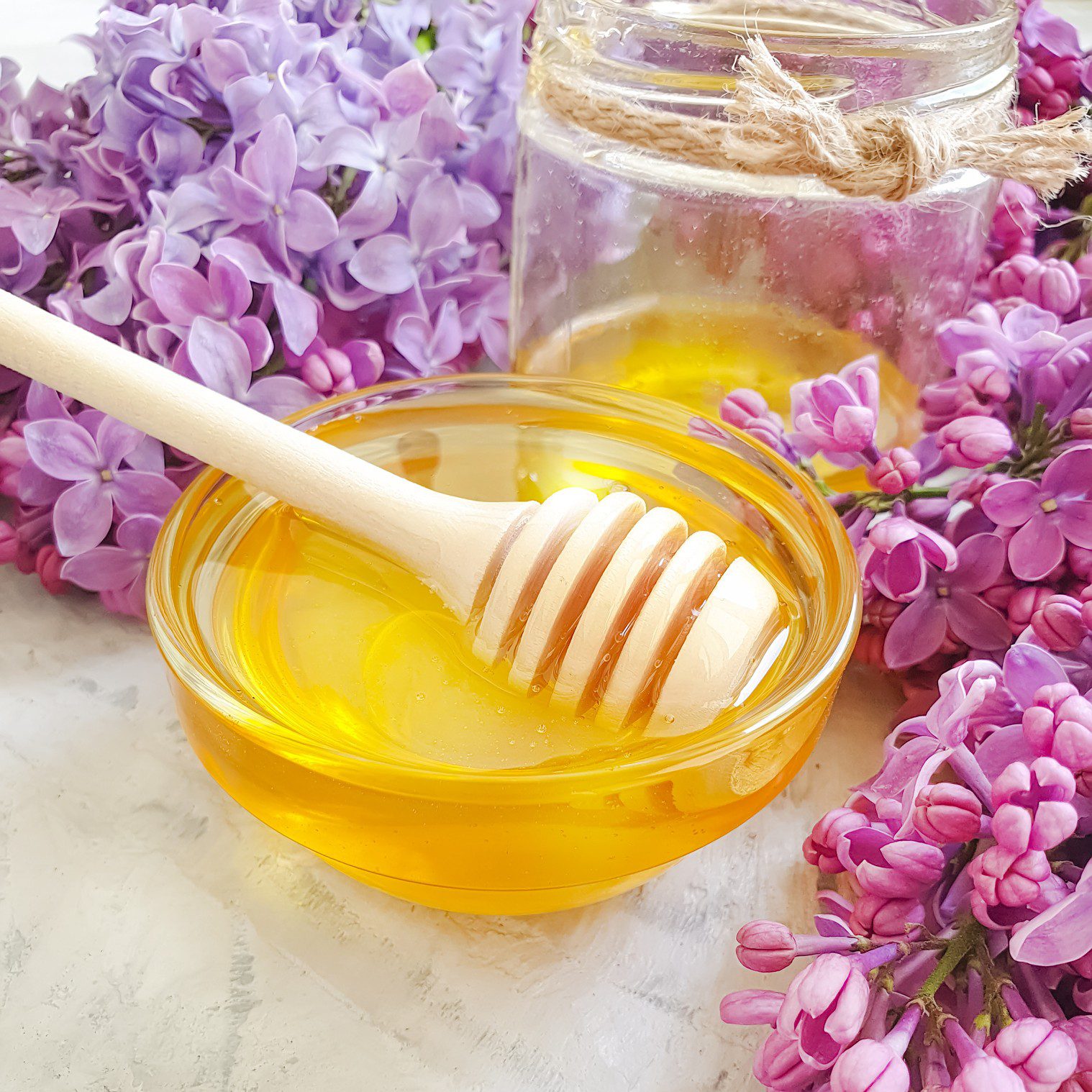 Honey dipper in bowl surrounded by lilacs.