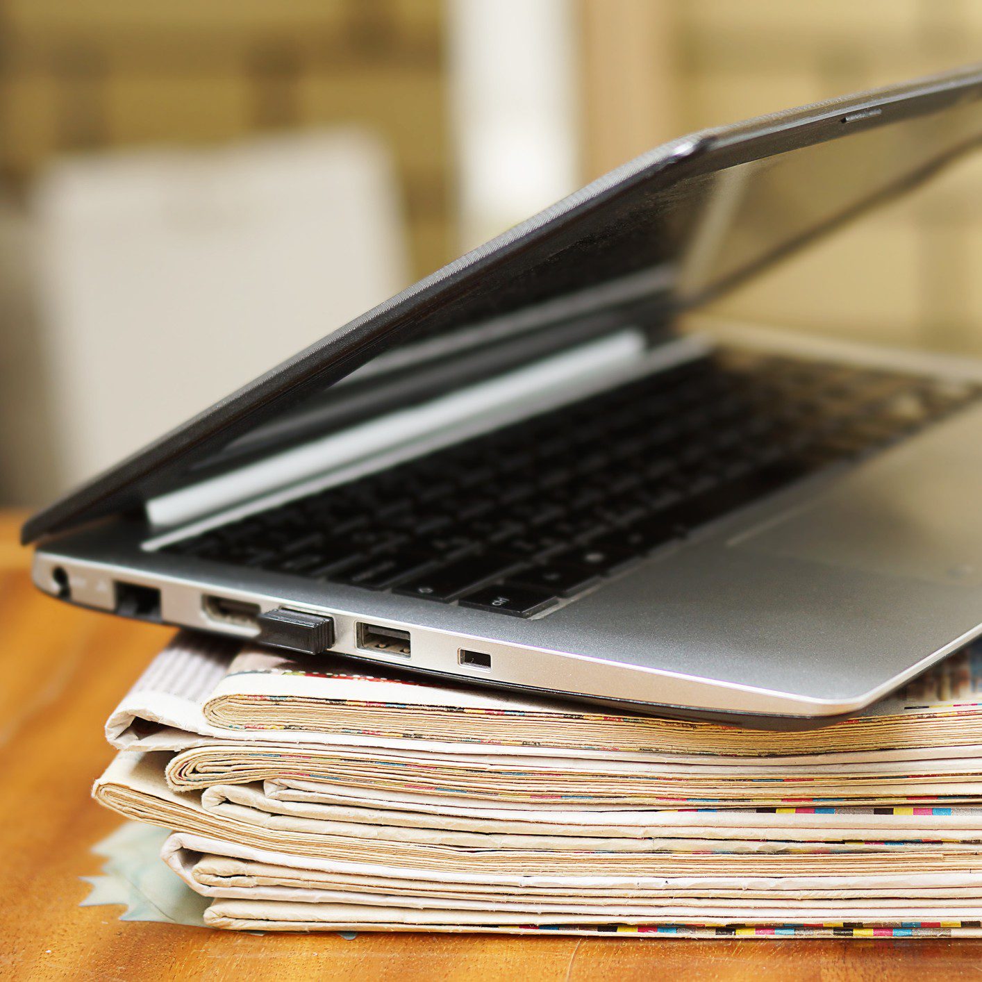 Laptop resting on stacked newspapers.