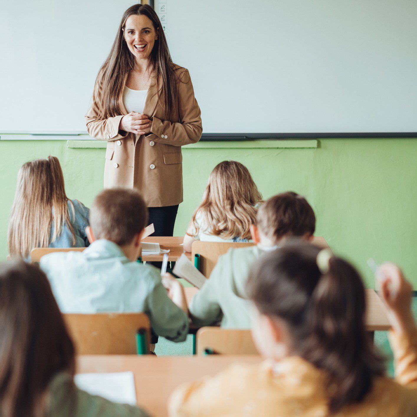 Teacher smiling in classroom with students seated.
