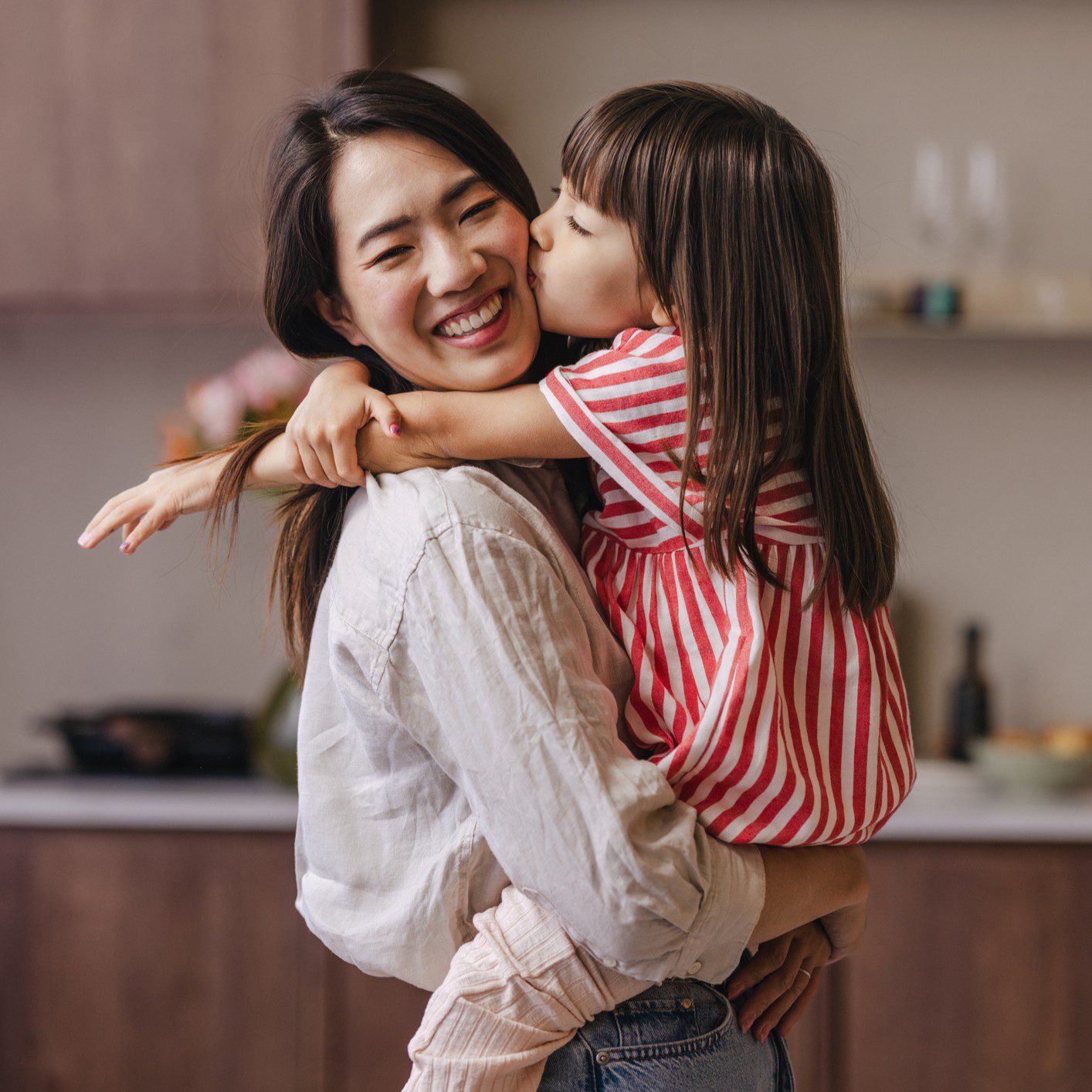 Mother and daughter hugging in kitchen.