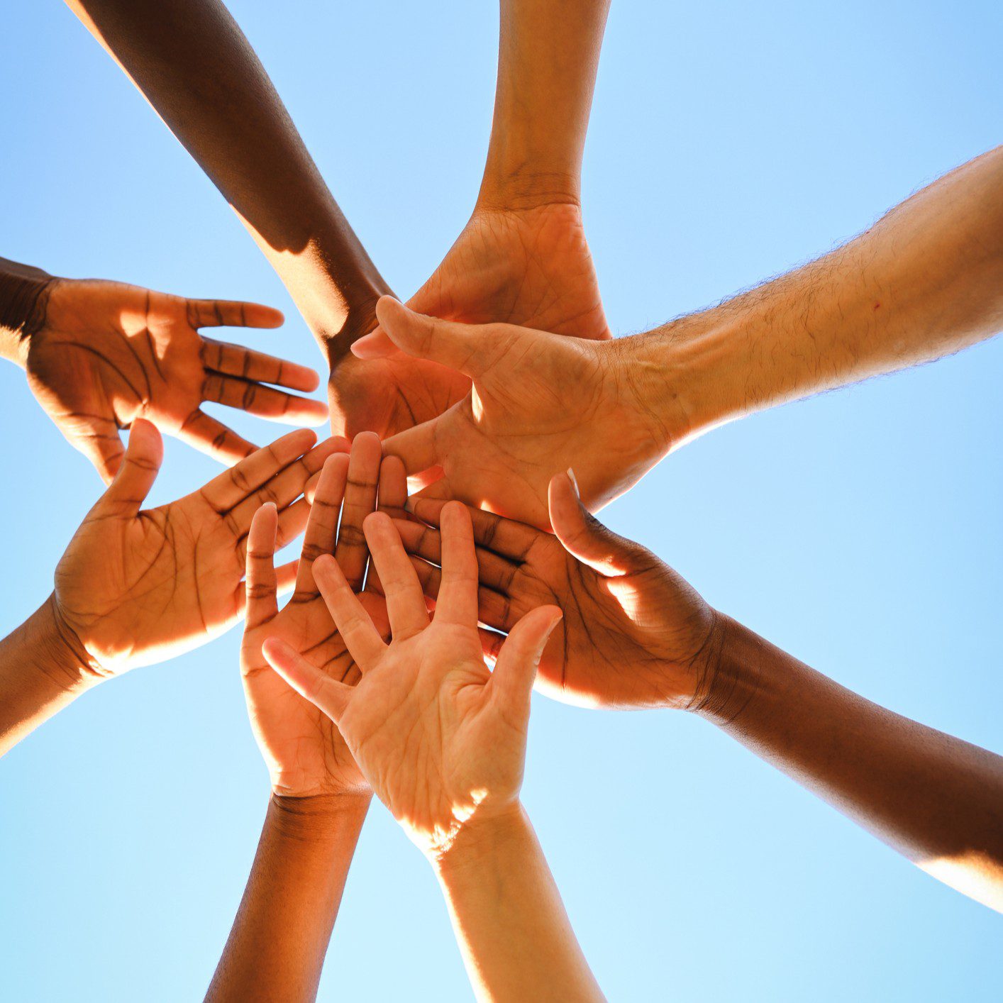 Diverse hands reaching together against blue sky.