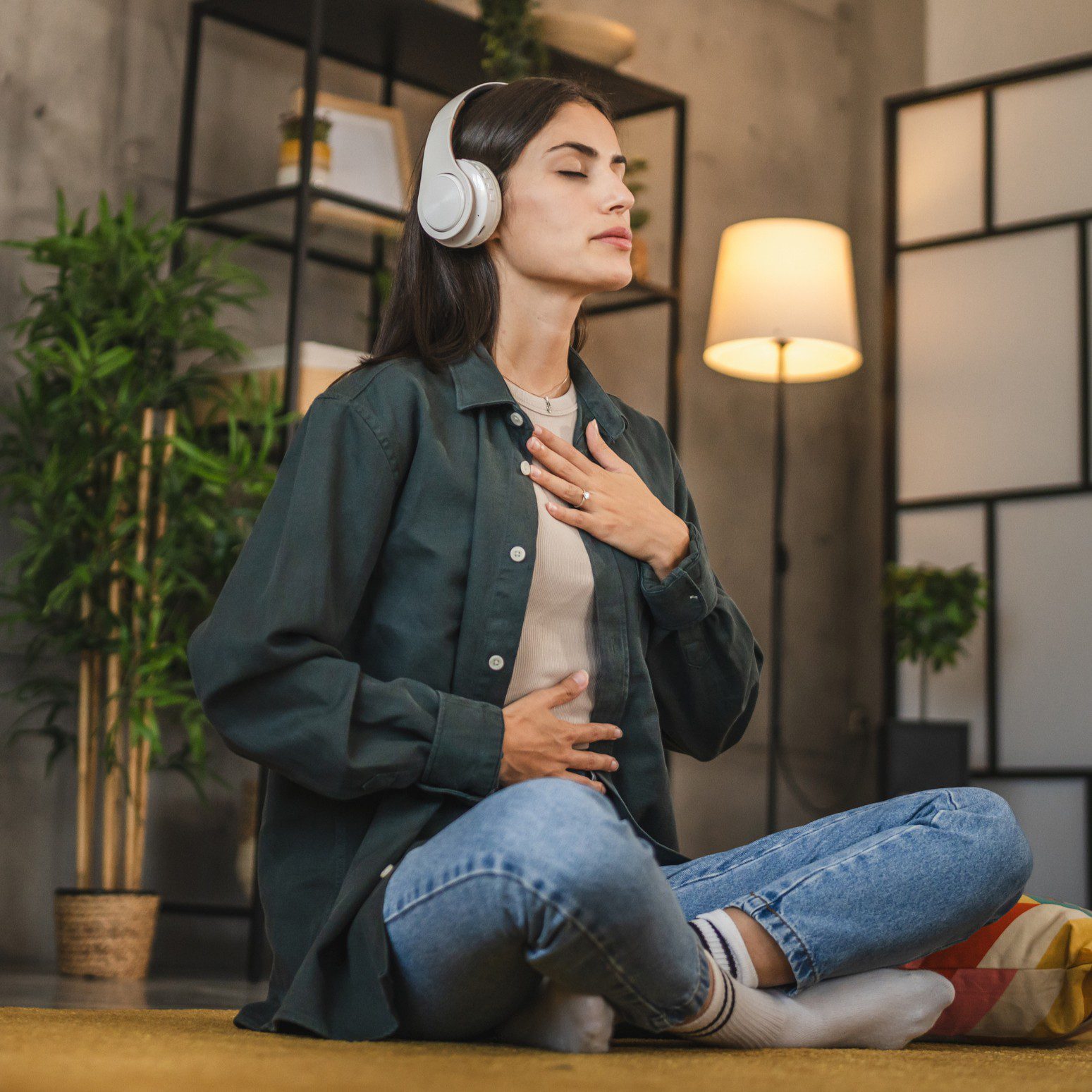 Woman meditating with headphones in living room.