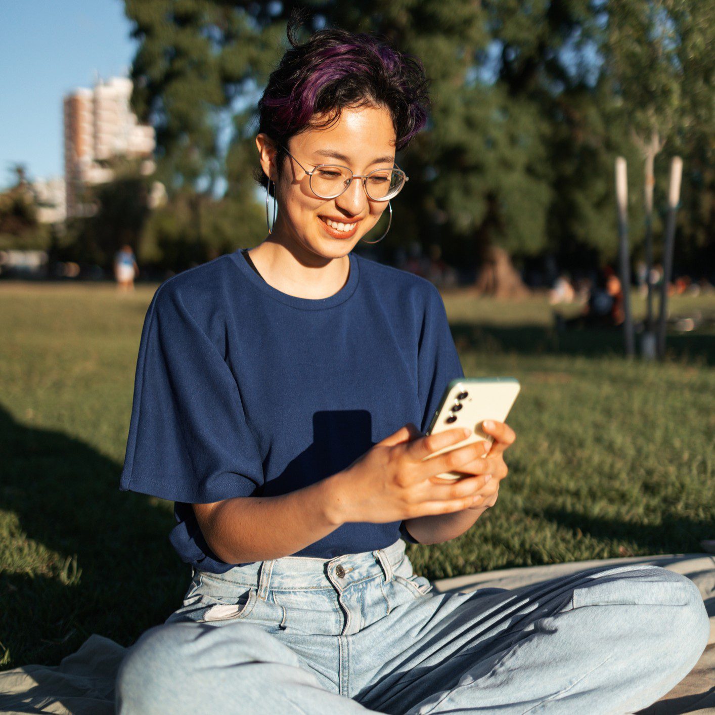 Person sitting on grass using smartphone outdoors.