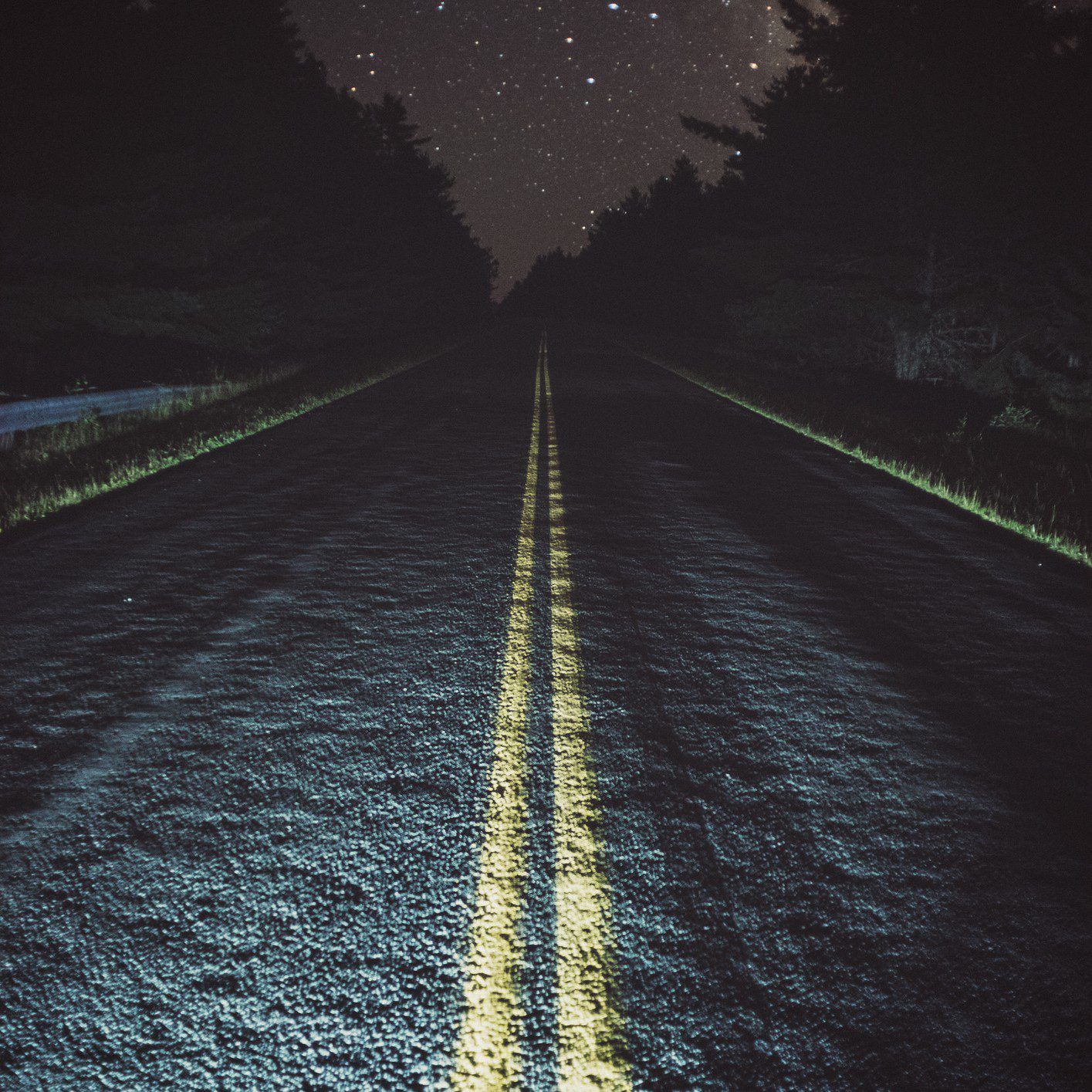 Night road under starry sky, lined trees.