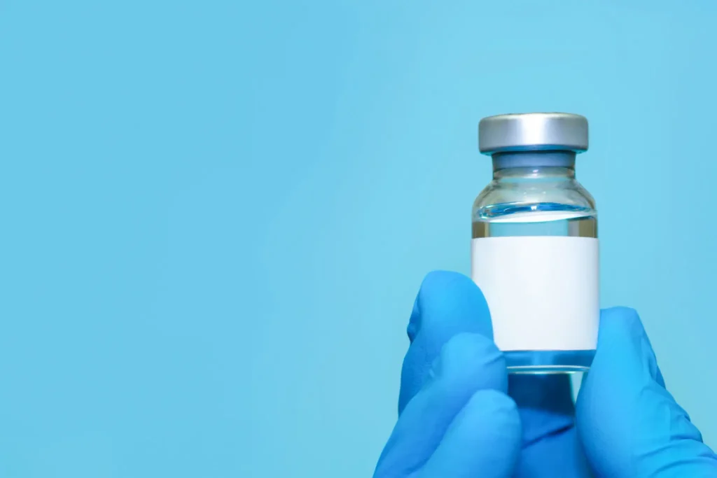 A gloved hand holding a vaccine vial against a blue background.