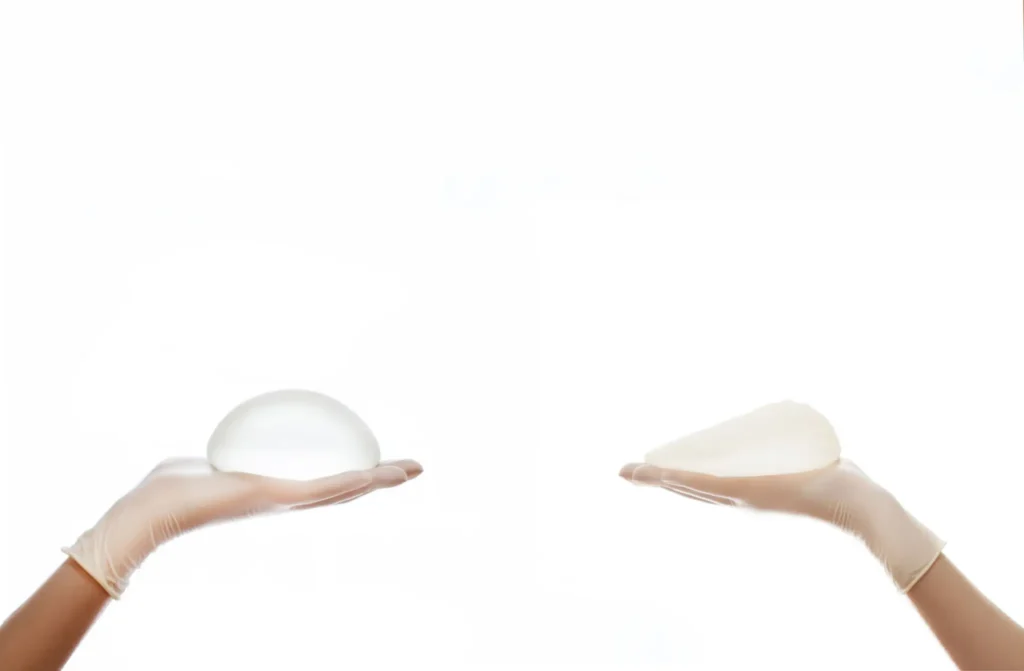 Two hands each holding a transparent silicone breast implant against a white background.
