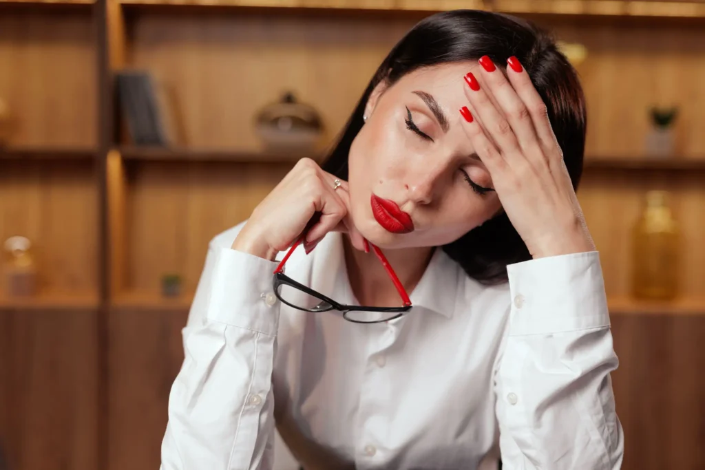 Tired woman holding glasses and touching her forehead in a cozy room.
