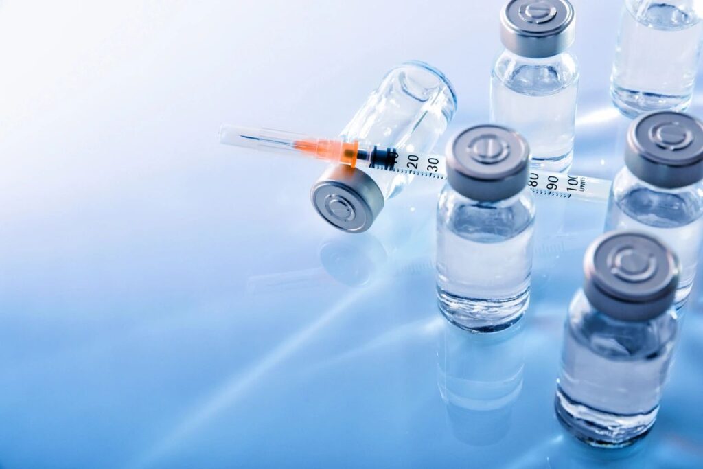 Medical syringes and vaccine vials on a reflective surface.
