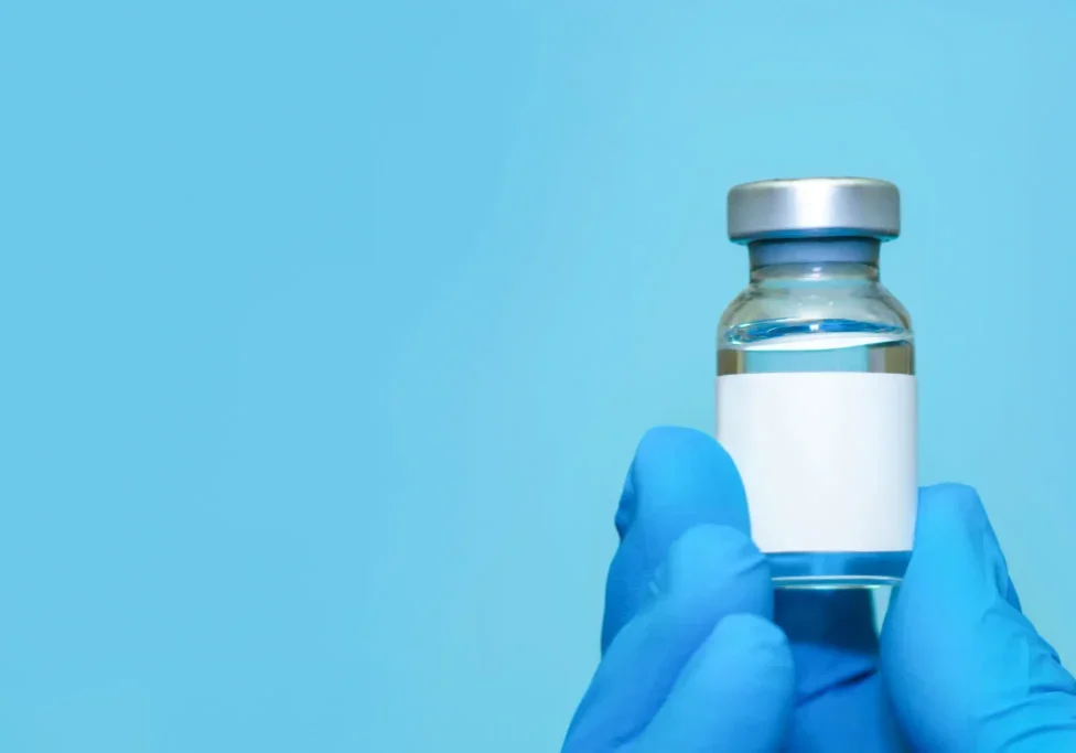 A gloved hand holding a vaccine vial against a blue background.