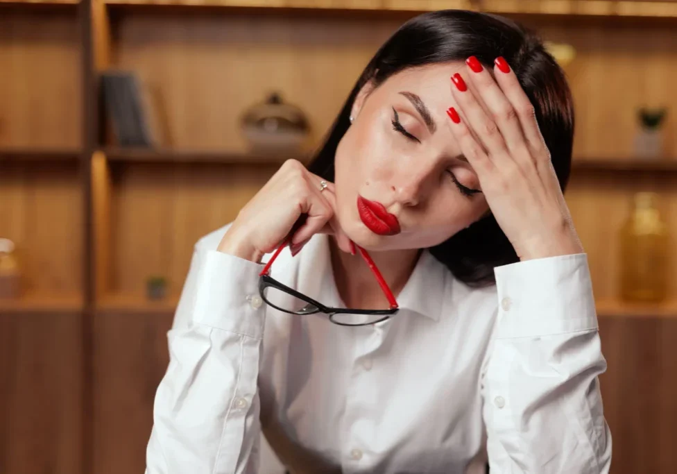Tired woman holding glasses and touching her forehead in a cozy room.