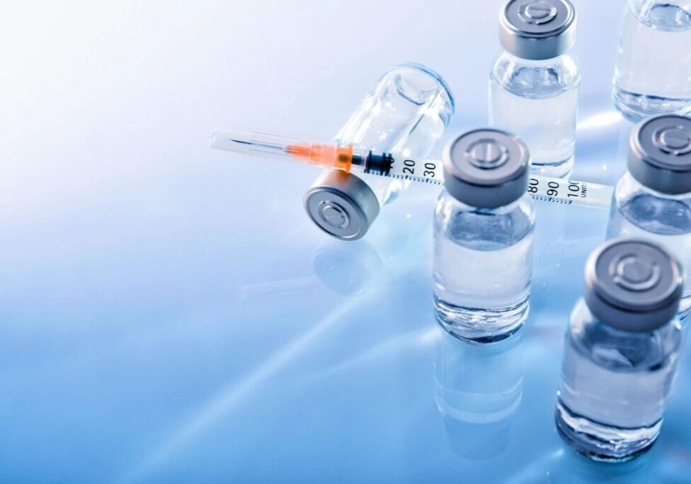 Medical syringes and vaccine vials on a reflective surface.